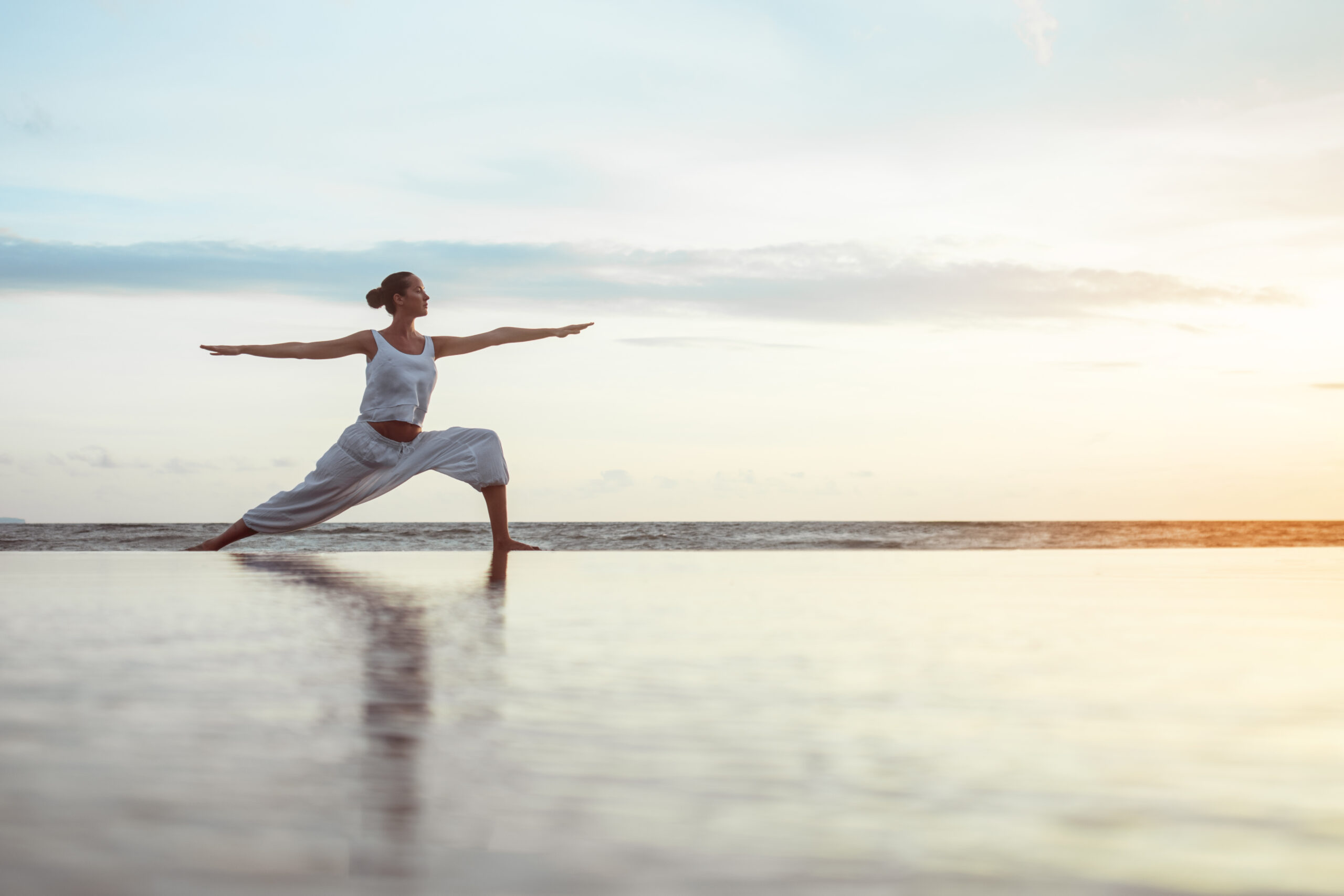 Bild zeigt eine Frau am Strand beim Yoga in der Pose des Kriegers