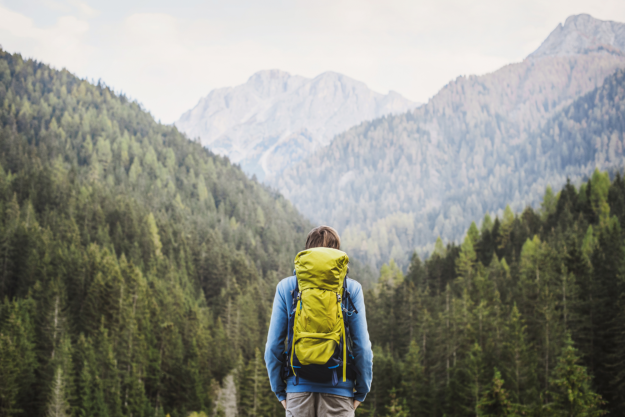 Young backpacking man traveler enjoying nature in Alps mountains Weiblicher Wanderer blickt von einem Berg in ein bewaldetes Tal